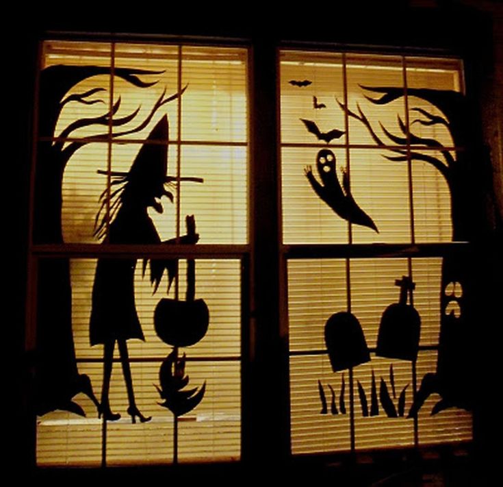 Silhouettes of witches and monsters taped to a window, glowing at night.