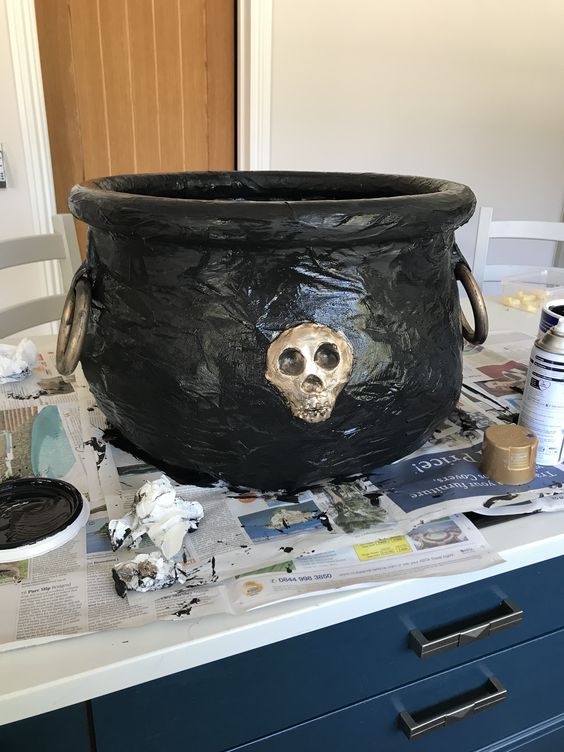 Cauldron decorated with small metallic-painted skulls for a gothic effect, ideal for Halloween or dark-themed décor.